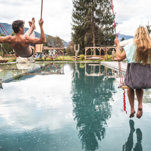 Couple swinging over the natural swimming pool