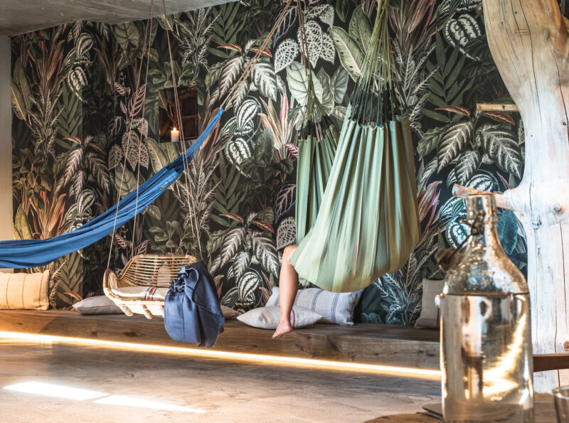 Frau liegt in Hängematte vor einer schönen Tapetenwand mit Dschungelmotiv im Flying Spa